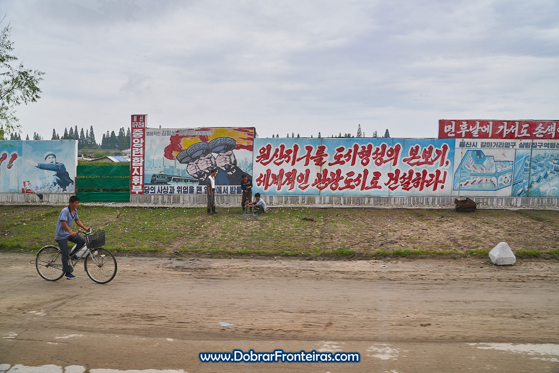 homem de bicicleta junto a cartazes de propaganda na Coreia do Norte